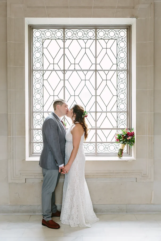 Bride and groom kiss in front of window