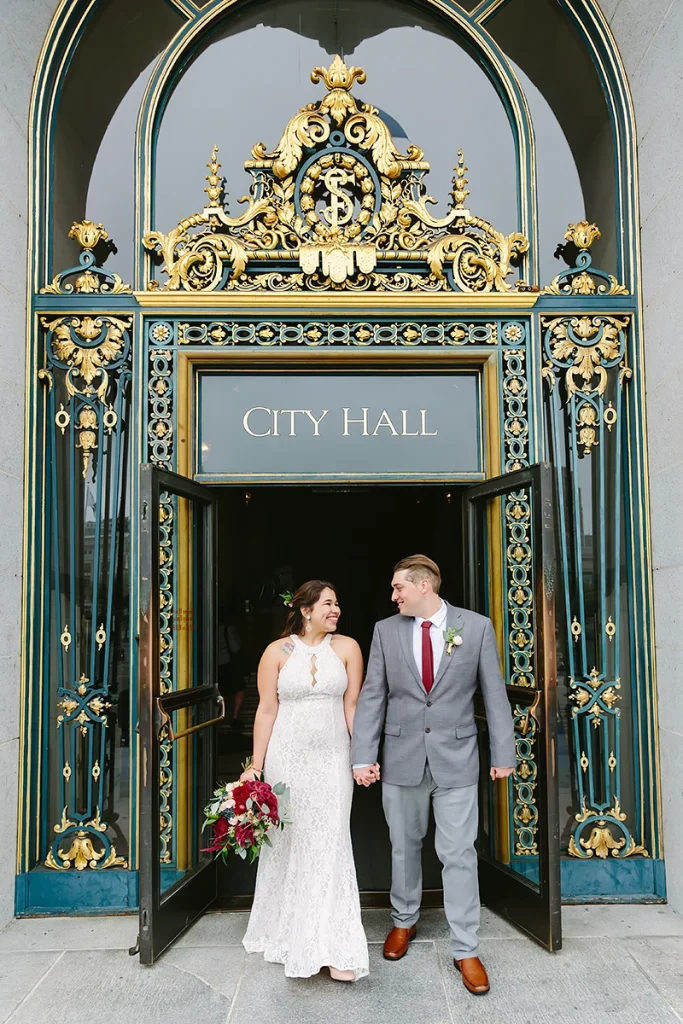 Bride and groom walk out the front doors of SF City Hall