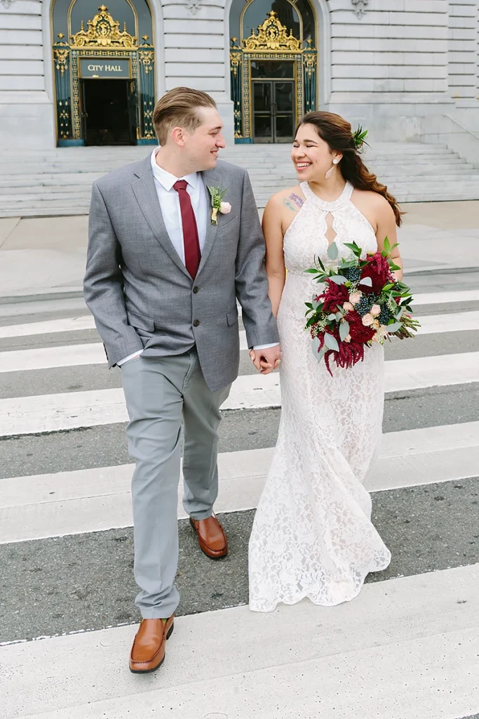 Bride and groom cross the street with San Francisco City Hall in the background