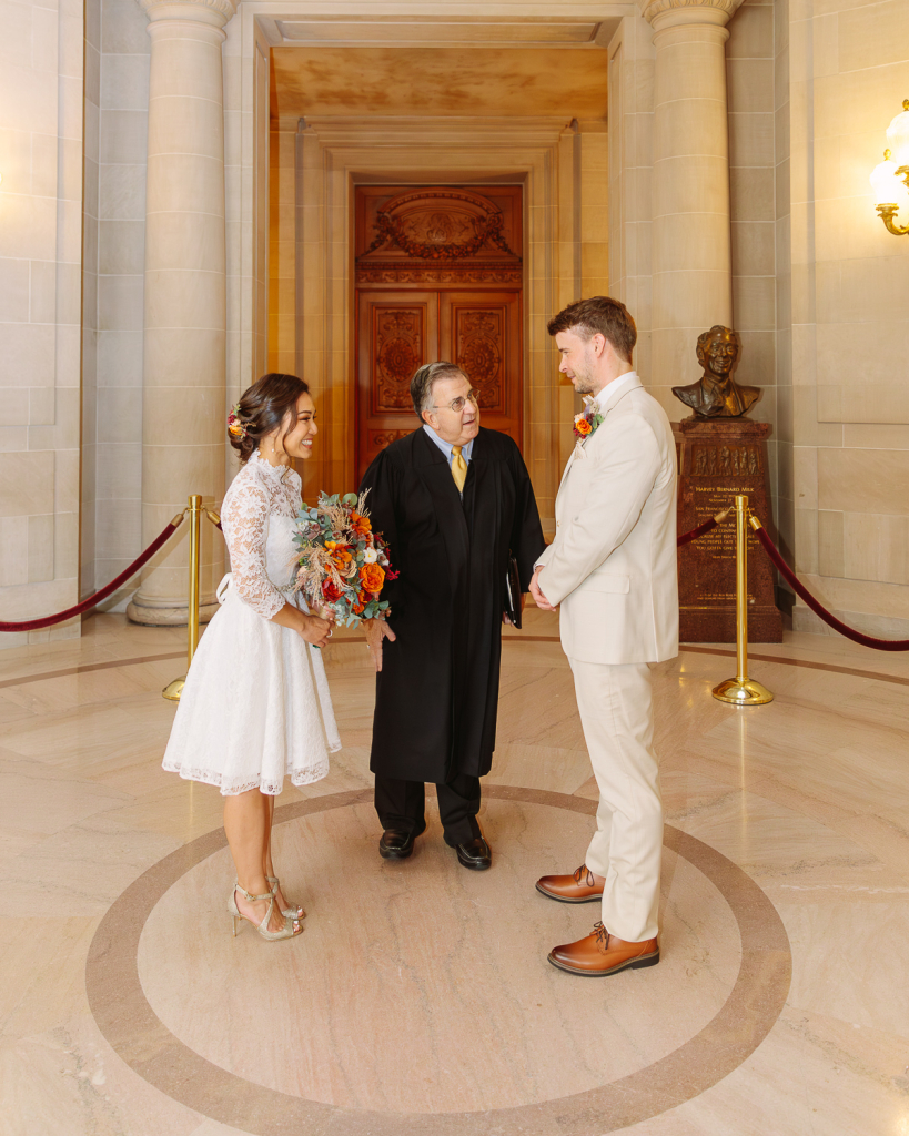 Couple laugh with ceremony officiant during their City Hall SF civil ceremony in Rotunda