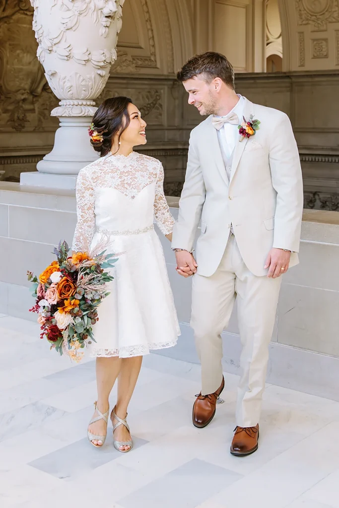 Couple hold hands and walk together at their City Hall SF wedding