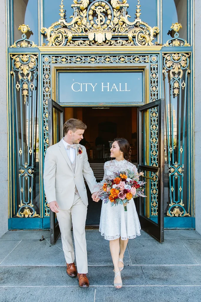 Couple hold hands as they walk out the front doors at their City Hall SF elopement