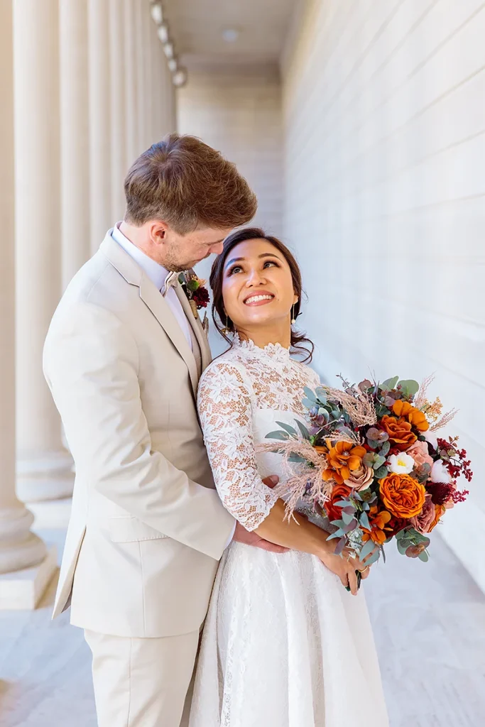Groom hugs bride from behind as she smiles at him