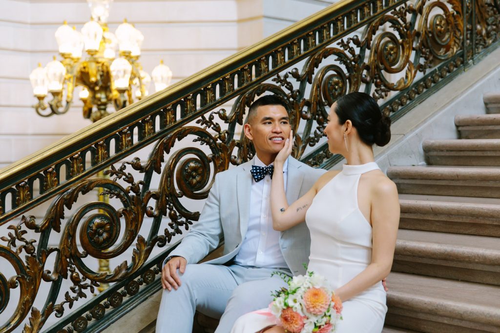 Bride caressing the face of her groom while they are both sitting on the Grand Staircase inside Wedding Ceremony on the Fourth Floor at San Francisco City Hall