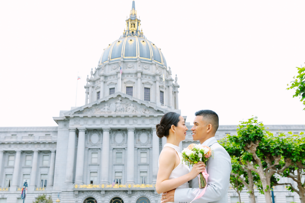 Bride and groom hug with San Francisco City Hall in the background