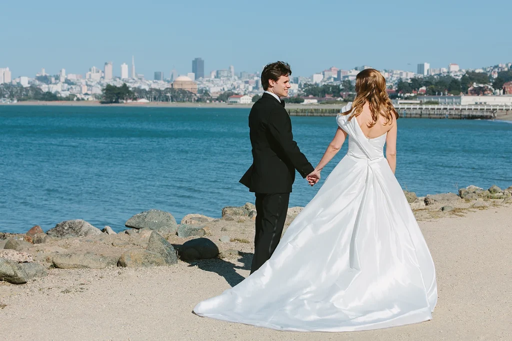 Bride and groom walk together with the San Francisco skyline in the background