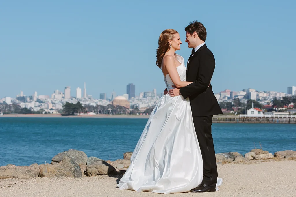 Bride and groom smile at each other with a view of the San Francisco skyline behind them