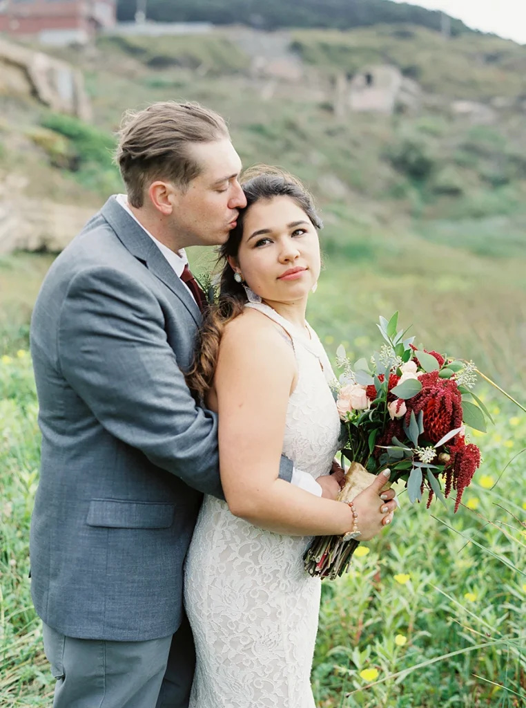 Groom embraces bride and kisses her forehead at their Sutro Baths wedding