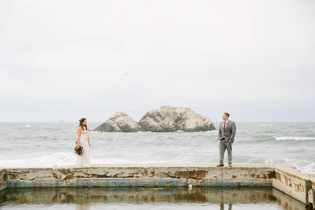 Couple stand apart with the Pacific Ocean in the background at their Sutro Baths wedding in San Francisco