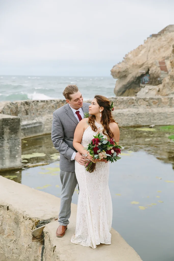 Groom holds bride with the ocean in the background